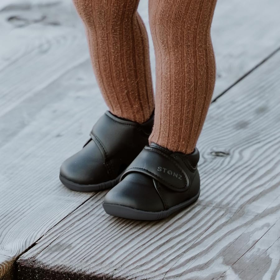 A toddler wearing black Stonz shoes